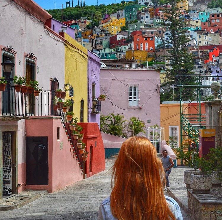 11 imprescindibles en México. a woman looks up at the colourful buildings on a hill in guanajuato