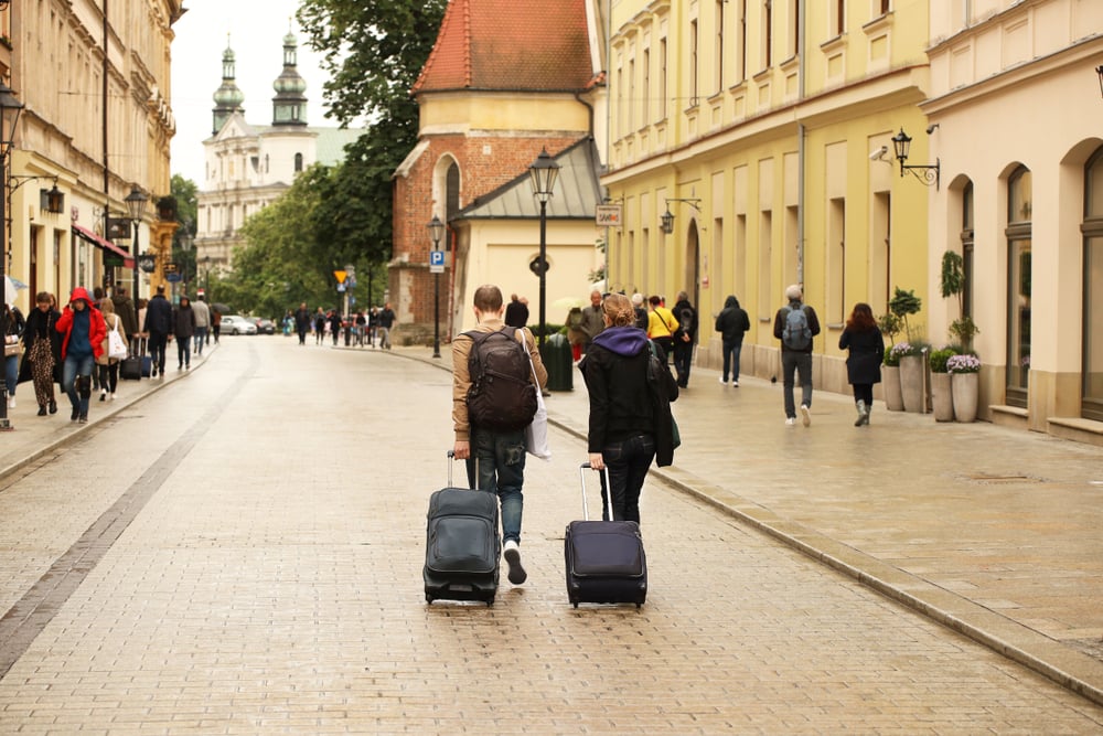 Two tourists walk carrying luggage in Krakow's city center, Poland